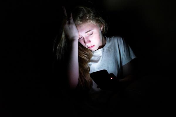 Upset girl sitting in the dark, her face illuminated by the light from her smartphone screen